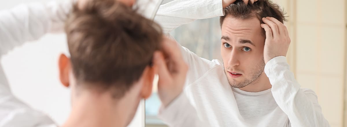 Ein junger Mann überprüft im Spiegel seine Haare nach Haarausfall