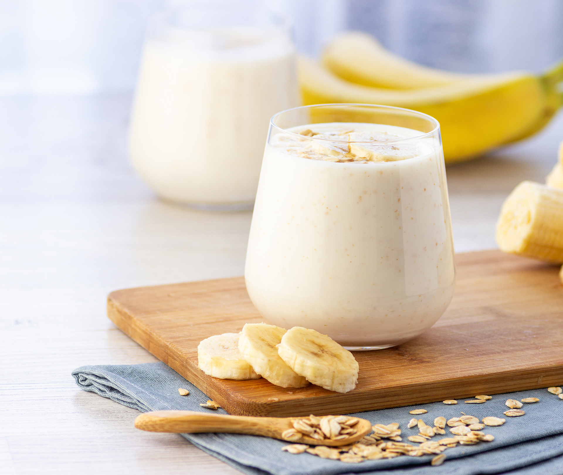 Glas mit Proteinshake auf einem Holzbrett mit Bananenscheiben drum herum