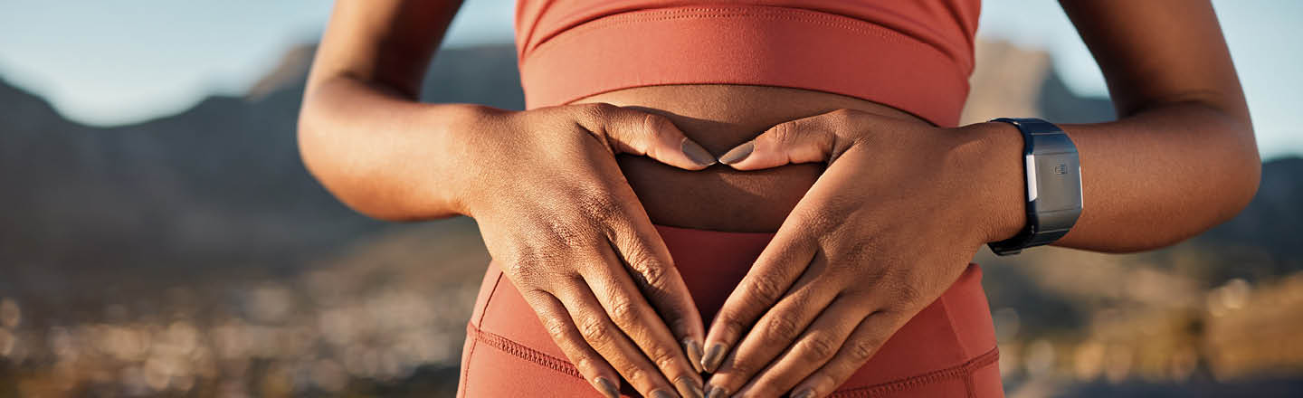 Sportlerin hält ihre Hände im Dreieck über Ihre Darmflora